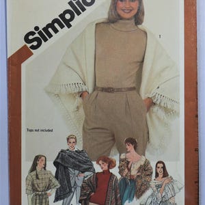 May include: Simplicity sewing pattern featuring a woman wearing a beige turtleneck, pants, and a fringed shawl. The pattern includes multiple garment designs, including tops and shawls. The text "Tops not included" is visible.