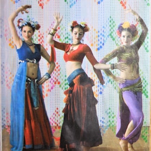 May include: Simplicity 3832 The Dance Studio sewing pattern envelope featuring three variations of dance costumes. The costumes include cropped tops, long skirts, and harem pants in blue, red, and purple with floral headpieces and jewelry.