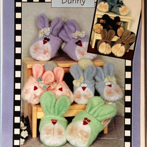May include: A variety of bunny-shaped slippers in pastel colors, including pink, purple, blue, and green. Each slipper features a white face, red nose, and bow. The image also includes a smaller inset image of similar slippers.