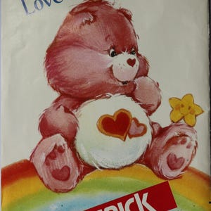 May include: A Butterick sewing pattern envelope for a Love-a-Lot Bear Care Bear, featuring a pink bear with two red hearts on its white belly, sitting on a rainbow and holding a yellow star. The text includes Care Bears, 6232, and MCMLXXXIII.
