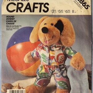 May include: McCall's Crafts pattern for a stuffed dog doll, featuring a plush dog wearing a colorful floral shirt and pants. A beach ball and a gray towel are in the background. The pattern number is 2865.