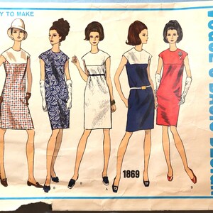 May include: Vintage Vogue Basic Design sewing pattern featuring five dress designs. The dresses are illustrated in various colors and patterns, including a red and white checkered print, a blue paisley print, and solid white, navy, and red options. The pattern number is 1869.