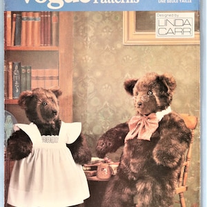 May include: Vogue Patterns 7572 sewing pattern envelope featuring two dark brown plush teddy bears. One bear wears a white pinafore with lace trim, while the other wears a pink bow tie and wire-rimmed glasses. Designed by Linda Carr.