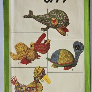 May include: Simplicity pattern 8779 featuring four stuffed animal designs: a whale, a duck, a turtle, and a creature with a red mouth. The animals are made from patterned fabric with floral and patchwork designs. The pattern is one size.