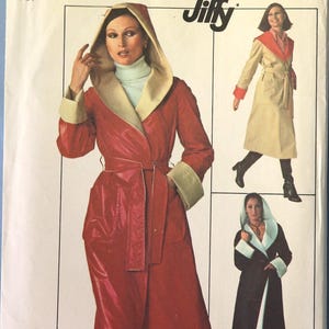May include: A Simplicity 7700 Jiffy sewing pattern envelope for a hooded robe or coat. The cover features illustrations of three variations of the garment in red, beige, and black with contrasting linings, including a tie belt and pockets.