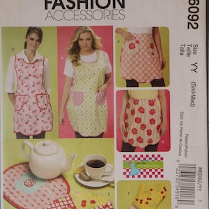 May include: McCall's Fashion Accessories M6092 sewing pattern envelope featuring illustrations of aprons, a teapot, a mug, a hot pad, and an oven mitt. The designs include floral, cherry, and checkered patterns in pink, green, red, and yellow colors.
