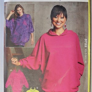 May include: A sewing pattern for misses' tops, featuring a woman wearing a pink hooded top. The pattern includes options for a cowl neck top and a yellow top. The pattern is labeled "KWIK SEW" and includes the size range XS-XL.