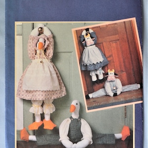 May include: Butterick pattern 4779 featuring a goose and cow doorstop design. The goose doorstop wears a floral dress and apron, while the cow doorstop has a blue dress. The pattern is designed by Wendy Everett.