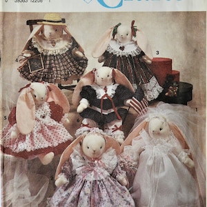 May include: Simplicity Crafts pattern featuring several plush bunny dolls in various outfits. The bunnies are dressed in dresses, bonnets, and a straw hat. One bunny holds a small chalkboard. The pattern is by Faith Van Zanten.