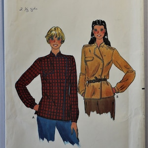 May include: A Butterick 6777 sewing pattern envelope featuring illustrations of two long-sleeved shirts. View A is a red and black plaid shirt with a high collar and button front. View B is a solid mustard yellow shirt with a belt and collar.
