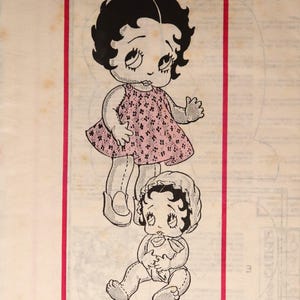May include: Black and white illustration of two Betty Boop figures within a red rectangular border. The top figure is standing and wearing a pink dress. The bottom figure is seated and wearing a bonnet. The text "DESIGN 675" is at the bottom.