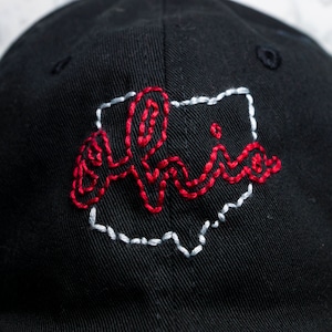 May include: Black baseball cap with embroidered Ohio state outline and the word "Ohio" in red thread. The hat is made of a durable fabric and features a curved brim. A stylish accessory for any Ohio fan.