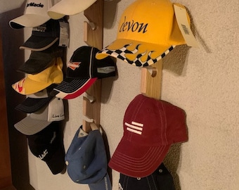 May include: A wooden hat rack with 10 baseball caps hanging on it. The caps are in various colors and designs, including yellow, red, blue, black, and white. Some of the caps have logos or text on them, such as "Devon" and "Titleist".