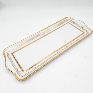 May include: A white rectangular serving tray with a gold decorative border. The border features a repeating pattern of stylized floral designs.