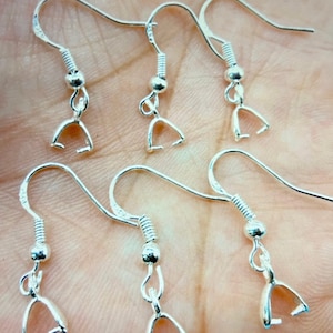 May include: Close-up of six silver-colored earring hooks. Each hook has a curved top, a coiled spring, a small bead, and a U-shaped clasp. The hooks are arranged against a blurred, light-colored background, suggesting a craft or jewelry-making theme.