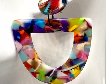 May include: A pair of colorful, multi-colored, abstract, geometric, resin earrings. The earrings are shaped like a U with a round, multi-colored, resin top.