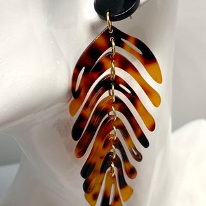 May include: A pair of long, brown and black tortoise shell earrings with a gold chain and a black circular top.