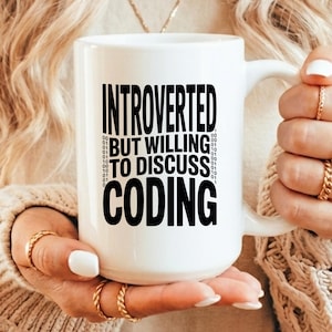May include: A white ceramic mug featuring the black text "INTROVERTED BUT WILLING TO DISCUSS CODING" printed on the front, flanked by vertical columns of binary code digits consisting of zeros and ones arranged in a clean, modern sans-serif font.