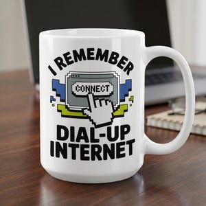 May include: A white ceramic mug featuring a black graphic print that reads I REMEMBER DIAL-UP INTERNET. The design includes a pixelated computer window with a CONNECT button and a white cursor hand icon in blue, green, and grey accents.