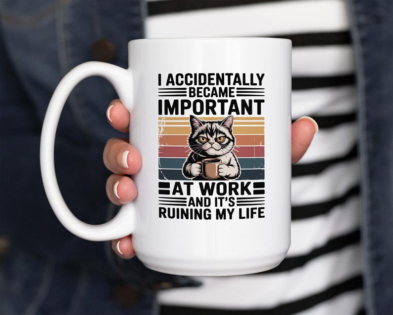 K&ouml;nnte beinhalten: Wei&szlig;e Keramik-Tasse mit schwarzem Henkel. Die Tasse zeigt eine Katze, die eine Kaffeetasse h&auml;lt, und den Text "I ACCIDENTALLY BECAME IMPORTANT AT WORK AND IT'S RUINING MY LIFE" in Schwarz.
