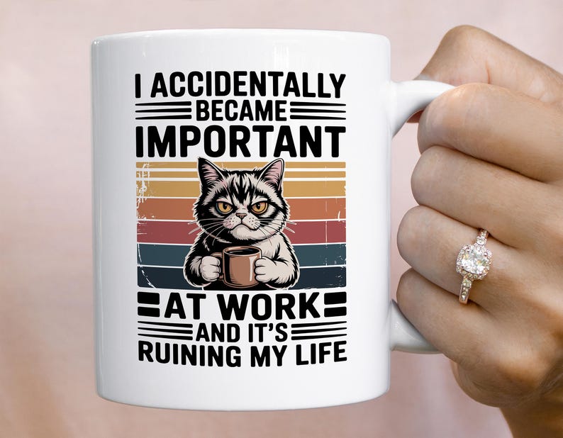 K&ouml;nnte beinhalten: Wei&szlig;e Keramiktasse mit einer Illustration einer grummeligen Katze, die eine Kaffeetasse h&auml;lt. Die Tasse tr&auml;gt den schwarzen Text "I ACCIDENTALLY BECAME IMPORTANT AT WORK AND IT'S RUINING MY LIFE" mit einem Retro-Farbblock-Design.