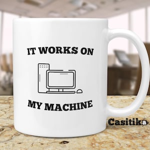May include: White ceramic coffee mug with a black outline of a computer and the text "IT WORKS ON MY MACHINE".
