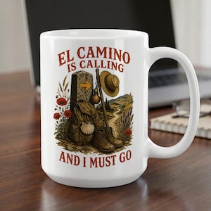 Pode incluir: Uma caneca de cerâmica branca com o texto EL CAMINO IS CALLING AND I MUST GO em letras castanhas. O gráfico mostra um marco de pedra com uma seta amarela, uma mochila, um cajado, um chapéu e papoilas vermelhas numa paisagem.