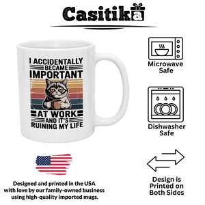 K&ouml;nnte beinhalten: Wei&szlig;e Keramik-Tasse mit Henkel, mit einer Katzenillustration, die eine Kaffeetasse h&auml;lt. Die Tasse tr&auml;gt den Text "I ACCIDENTALLY BECAME IMPORTANT AT WORK AND IT'S RUINING MY LIFE". Mikrowellen- und sp&uuml;lmaschinenfest.