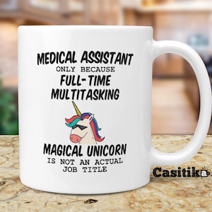 Pode incluir: Caneca de café de cerâmica branca com um gráfico preto e branco de um unicórnio usando óculos de sol. O texto na caneca diz "Medical Assistant Only Because Full-Time Multitasking Magical Unicorn Is Not An Actual Job Title".