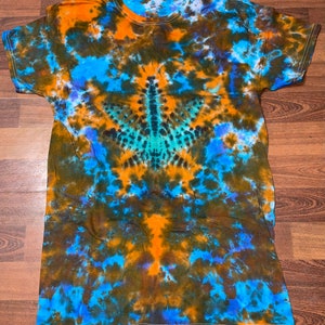 May include: A tie-dye t-shirt with a blue, orange, and green color scheme. The shirt has a unique pattern that resembles a leaf.