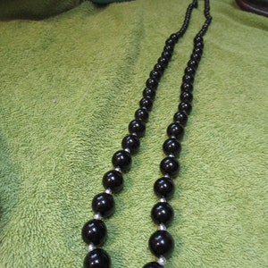 May include: A black beaded necklace with silver accents. The beads are large and round, and the necklace is strung on a silver chain.