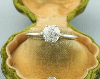 Könnte beinhalten: Ein Verlobungsring mit einem runden Brillanten, der in eine Weißgoldfassung gefasst ist. Der Ring befindet sich in einer grünen Samt-Ringbox.