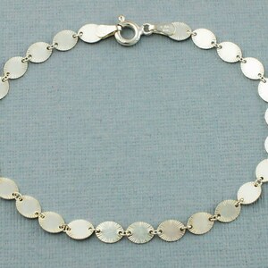 May include: A silver bracelet featuring a series of small, round, textured discs linked together. Each disc has a sunburst pattern radiating from the center. The bracelet is secured with a clasp.