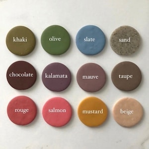 May include: Twelve round clay paint samples with color names written in white text. The colors are khaki, olive, slate, sand, chocolate, kalamata, mauve, taupe, rouge, salmon, mustard, and beige.