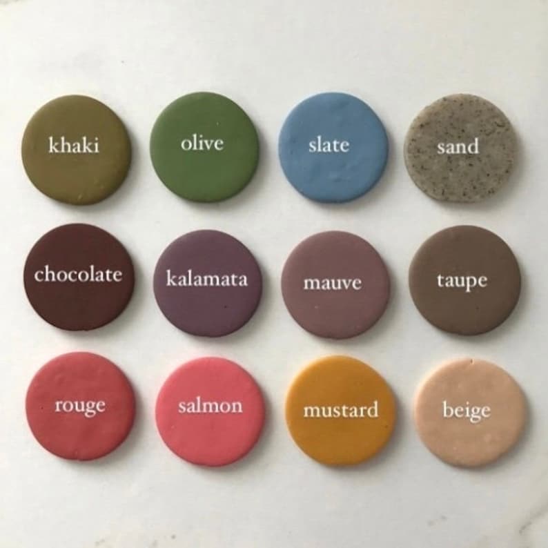 May include: Twelve round clay paint samples with color names written in white text. The colors are khaki, olive, slate, sand, chocolate, kalamata, mauve, taupe, rouge, salmon, mustard, and beige.