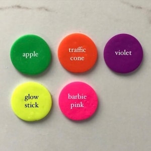 May include: Six round, colorful, plastic tokens with white text. The tokens read "apple", "traffic cone", "violet", "glow stick", "barbie pink", and "violet".
