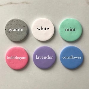 May include: Six round, flat, ceramic tiles with different colors and names. The colors are white, gray, light green, pink, lavender, and light blue. The names are "white", "granite", "mint", "bubblegum", "lavender", and "cornflower".