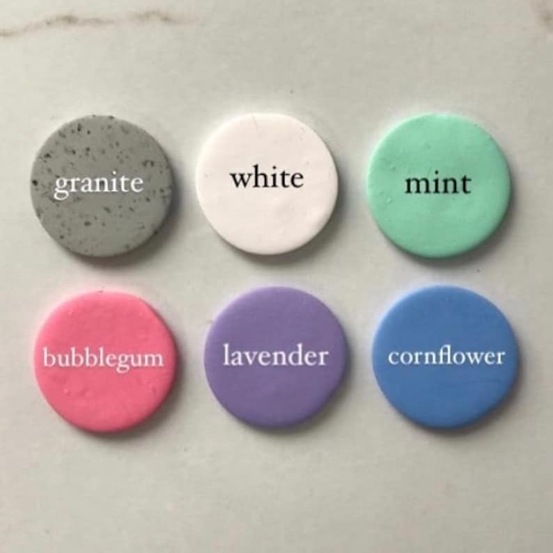 May include: Six round, flat, ceramic tiles with different colors and names. The colors are white, gray, light green, pink, lavender, and light blue. The names are "white", "granite", "mint", "bubblegum", "lavender", and "cornflower".