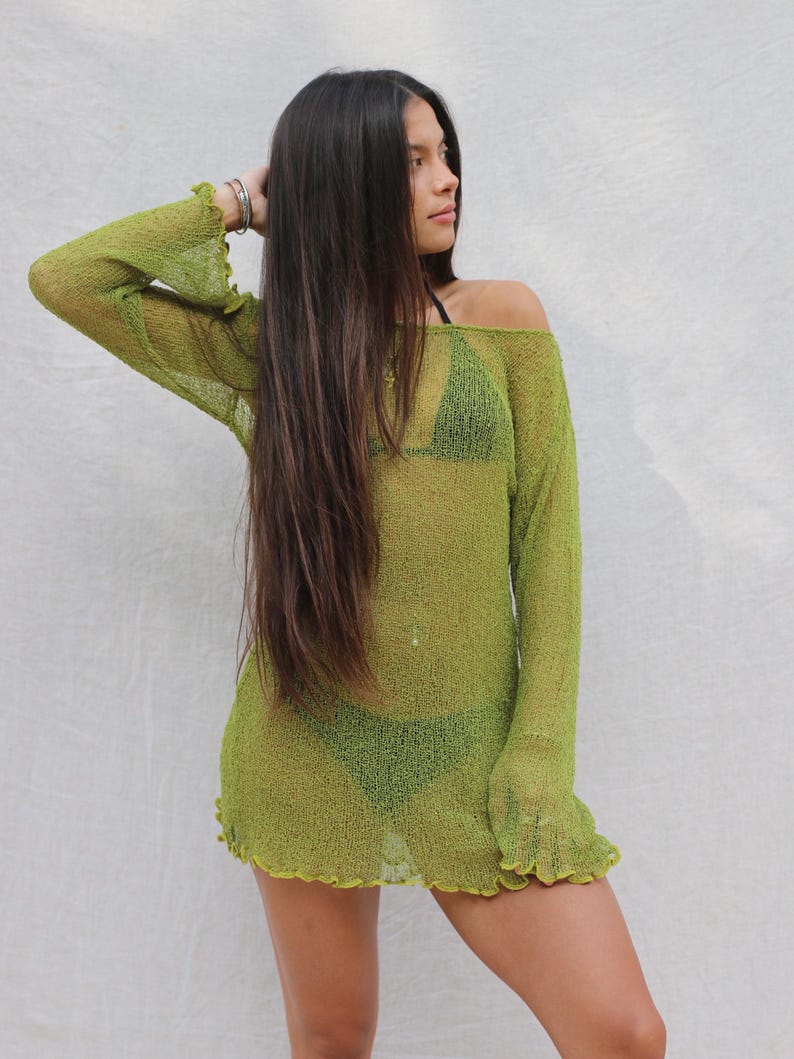 May include: A lime green, off-the-shoulder cover-up dress with long sleeves and a ruffled hem. The see-through knit fabric reveals a green bikini underneath. The model has long, dark hair.