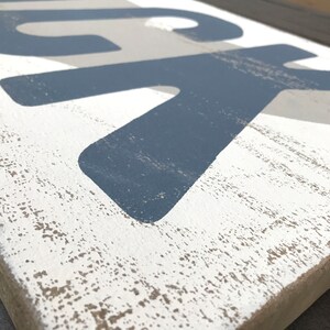 May include: A wooden sign with the word "LUCK" painted in blue and gray on a white background. The sign has a distressed, rustic look.
