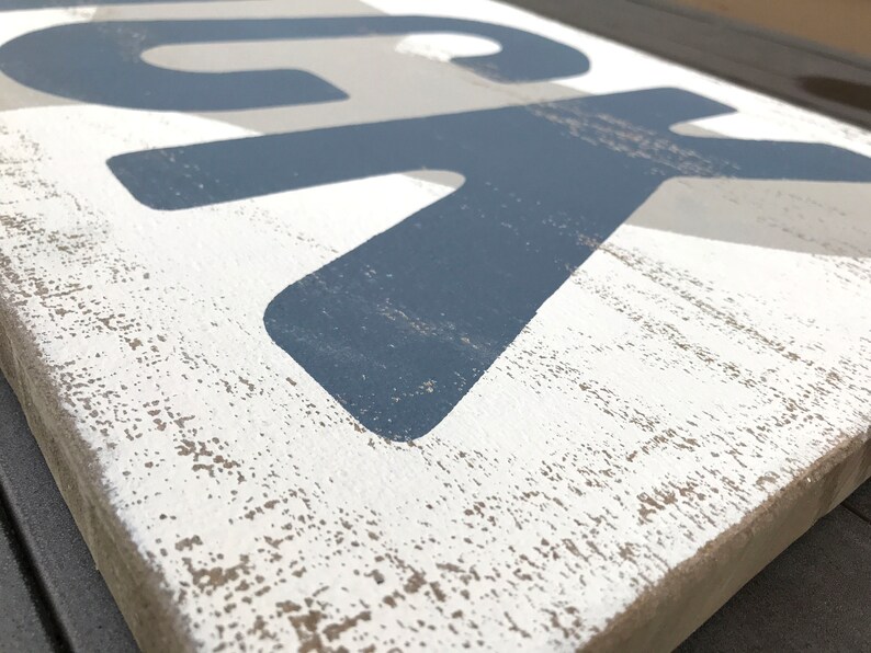 May include: A wooden sign with the word "LUCK" painted in blue and gray on a white background. The sign has a distressed, rustic look.