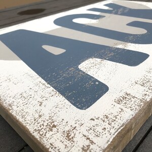 May include: A wooden sign with the word "ACE" painted in blue on a white background. The sign has a distressed, rustic look with a light brown stain.
