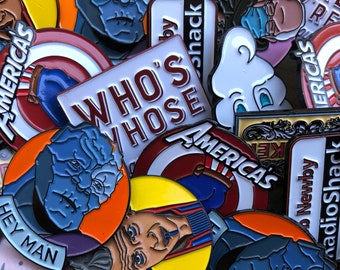 Peut inclure: Une collection d'épingles émaillées avec divers motifs. Certaines épingles présentent des portraits, tandis que d'autres affichent du texte comme "WHO'S WHOSE" et "HEY MAN". La palette de couleurs comprend le bleu, le rouge, le jaune et le blanc. Les épingles sont probablement des objets de collection.