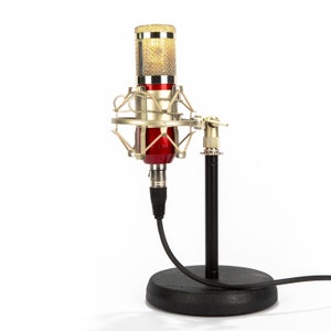 Peut inclure: Un microphone à condensateur doré et rouge avec un filtre anti-pop et un pied noir. Le microphone est relié au pied par un câble noir.
