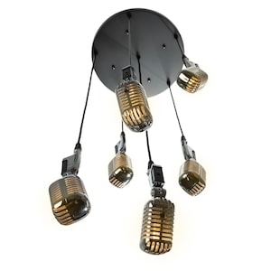 May include: A black ceiling fixture with six vintage-style microphones hanging from it. The microphones are silver with gold accents and have a warm, yellow light emanating from them.