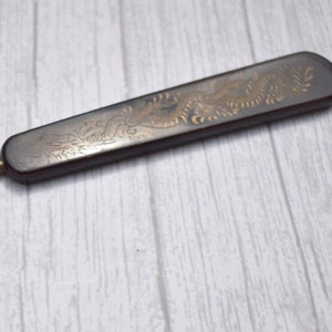 Può includere: Un calzascarpe in metallo marrone con un design a forma di drago dorato. Il calzascarpe ha un gancio a un'estremità e un manico all'altra.