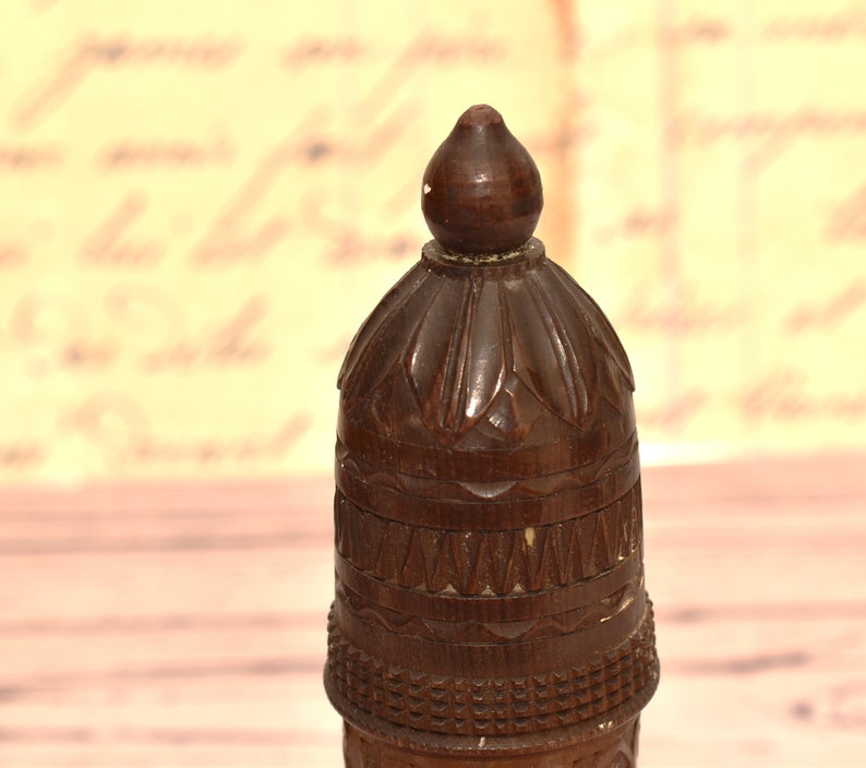 May include: A dark brown wooden bottle stopper with intricate carvings. The top of the stopper is shaped like a dome with a pointed tip.