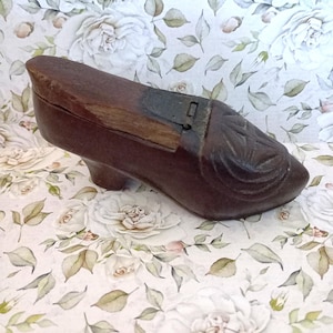 May include: A dark brown, wooden shoe-shaped box with a carved floral design on the toe. The box has a small heel and a hinged lid with a metal clasp. The box is likely vintage and decorative.
