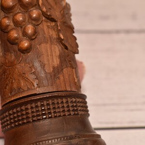 May include: A wooden bottle stopper with a carved grape design. The stopper has a detailed carving of grapes and leaves, and a decorative band around the bottom.