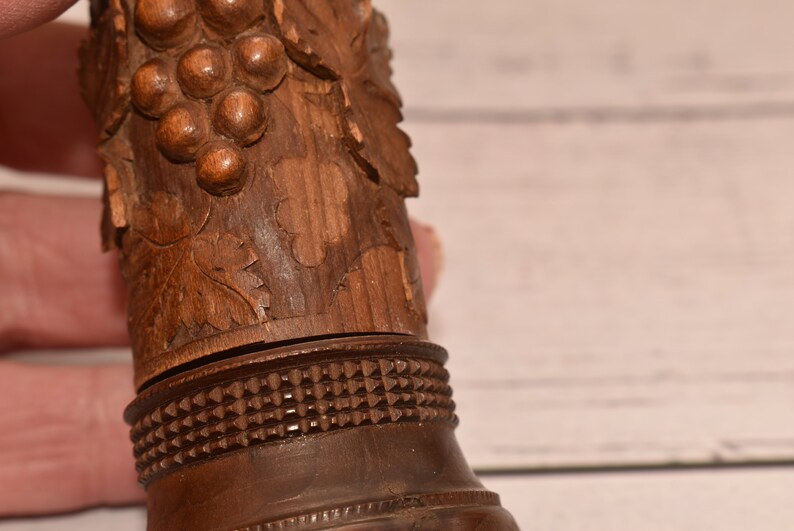 May include: A wooden bottle stopper with a carved grape design. The stopper has a detailed carving of grapes and leaves, and a decorative band around the bottom.